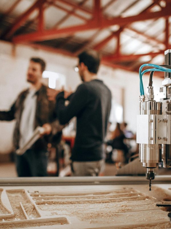 Three men discussing work in a woodworking shop with CNC machinery in focus.